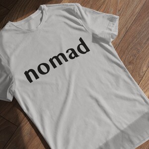 May include: A white t-shirt with the word "nomad" printed in black on the front.