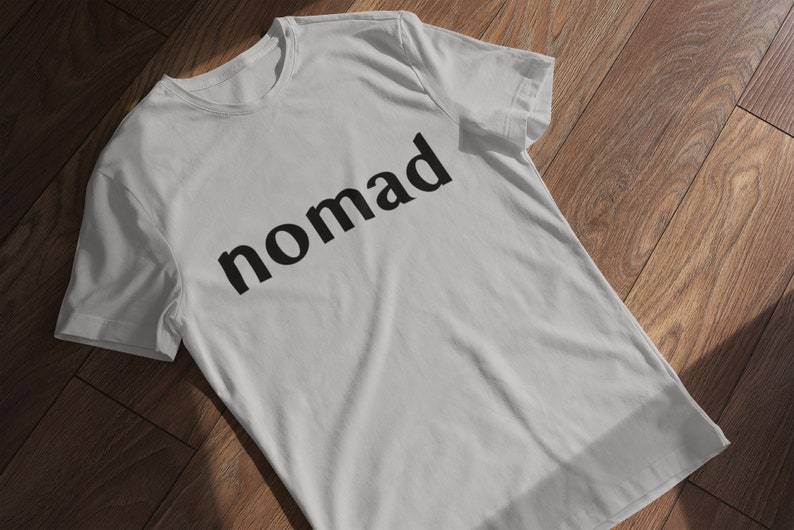 May include: A white t-shirt with the word "nomad" printed in black on the front.