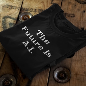 May include: Black t-shirt with the text "The Future Is A.I." in white, displayed on a wooden surface. The shirt is folded, showcasing the crew neck and the printed message. The background features a rustic wooden table.