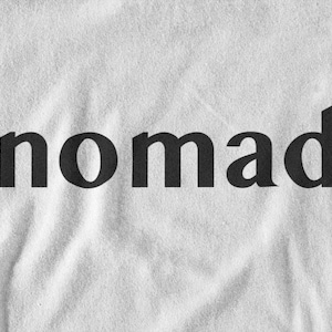 May include: A white t-shirt with the word "nomad" printed in black.