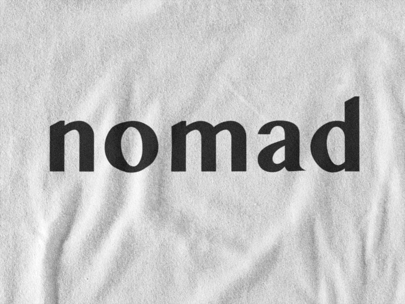 May include: A white t-shirt with the word "nomad" printed in black.