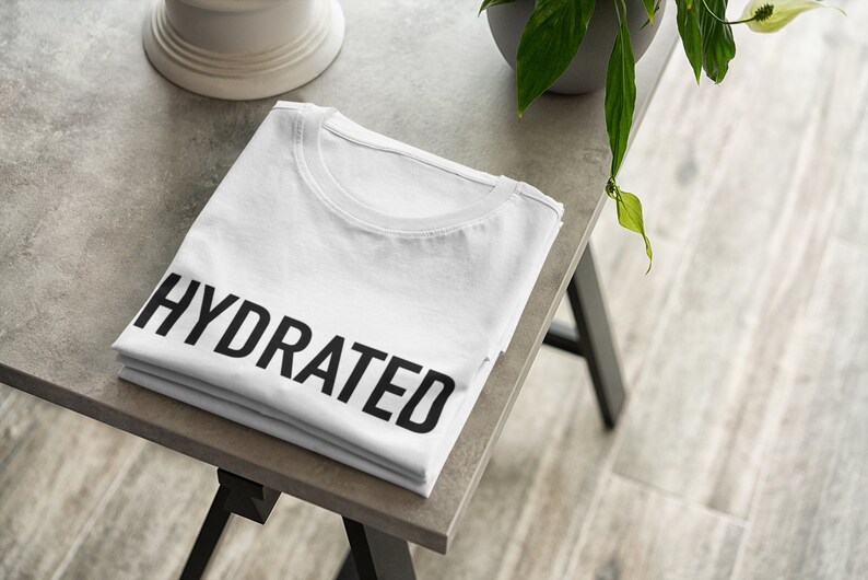 May include: A white t-shirt folded on a gray table with the word "HYDRATED" printed in black on the front.