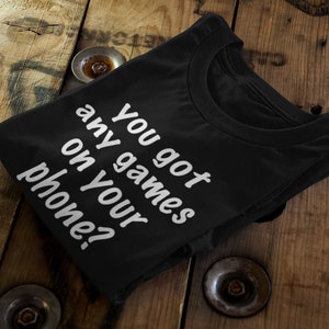 Puede incluir: Camiseta negra con texto blanco que dice "¿Tienes juegos en tu teléfono?"