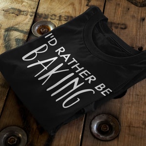 Peut inclure: T-shirt noir avec du texte blanc qui dit "J'aimerais mieux être en train de cuisiner".