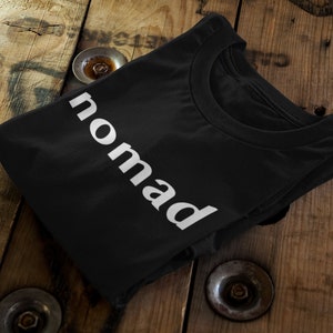 May include: Black t-shirt with the word "nomad" printed in white on the front.