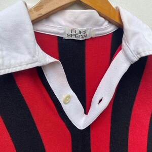May include: A vintage collared shirt with bold red and black vertical stripes. The shirt features a white collar and placket with a single button closure. The label reads "FLIPS SPECIAL".