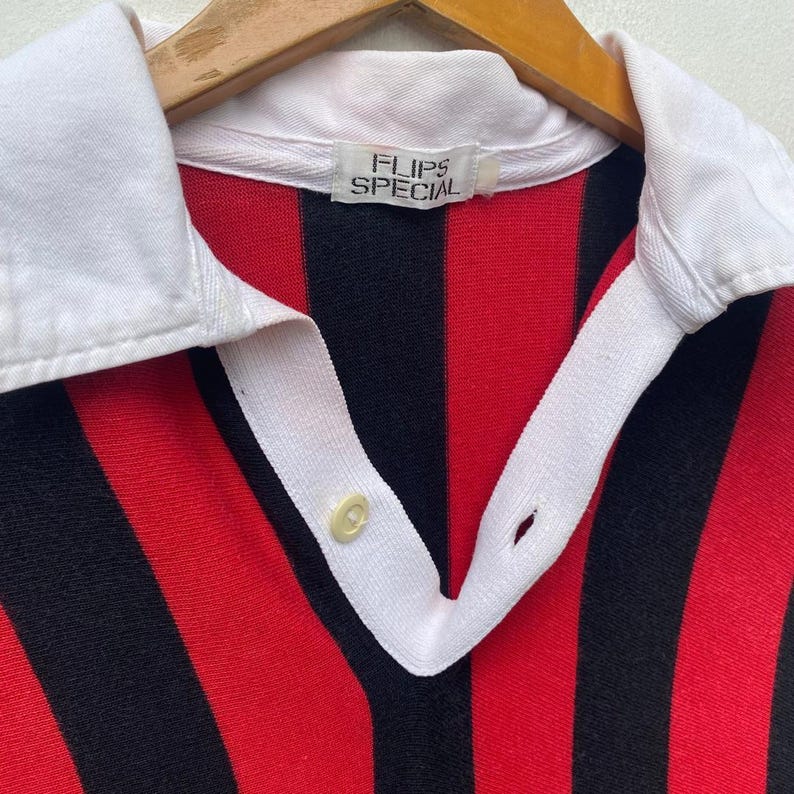 May include: A vintage collared shirt with bold red and black vertical stripes. The shirt features a white collar and placket with a single button closure. The label reads "FLIPS SPECIAL".