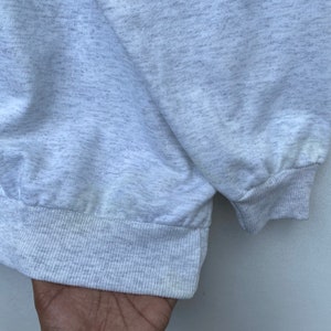 May include: Close-up of the bottom hem of a gray sweatshirt with a ribbed cuff.