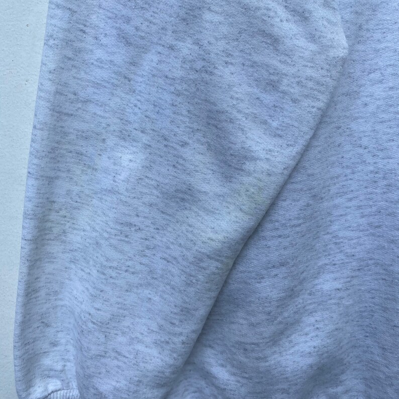 May include: A close-up of a gray sweatshirt with a slightly textured surface. The fabric appears to be soft and comfortable.