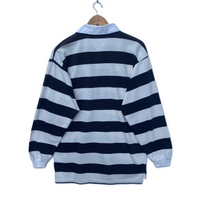 May include: A long-sleeved rugby shirt with white and black horizontal stripes. The shirt has a collared neckline and a button closure.
