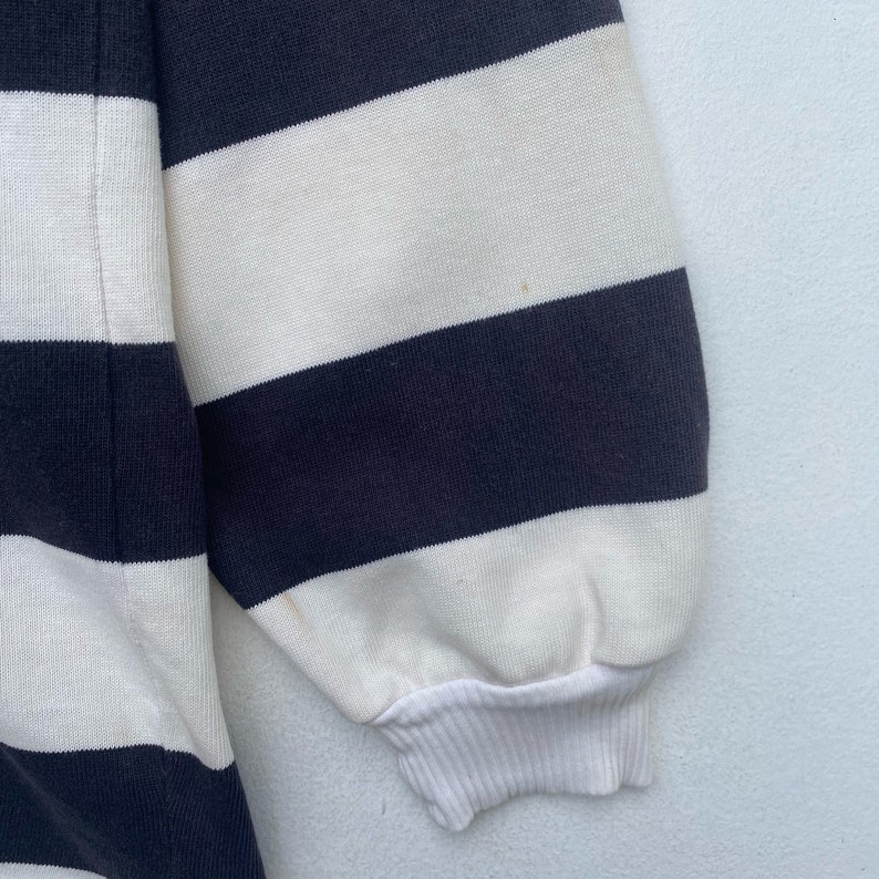 May include: Close-up of the sleeve of a striped sweater. The sweater is white and navy blue with a ribbed cuff.