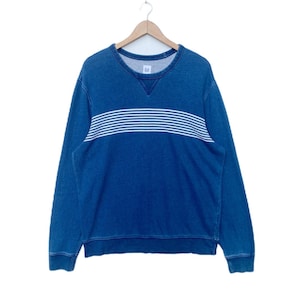 May include: A blue long-sleeved sweatshirt with a white horizontal striped band across the chest. The sweatshirt has a crew neck and the word "GAP" is visible on the inside of the neck.