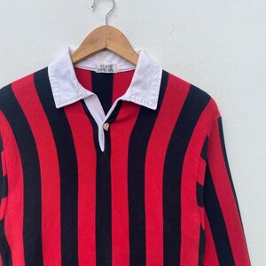 May include: A red and black striped long-sleeve shirt with a white collar. The shirt has a button-down placket and the text "FLIPS SPECIAL" is visible on the collar. The shirt is hanging on a wooden hanger.