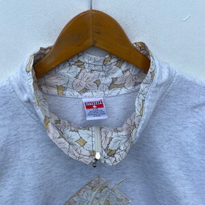 May include: A gray sweatshirt with a zipper and a floral print lining the collar. The label reads "CITYSCAPE" and includes the size "L/XL" and the fabric content "100% COTTON / COTON 100%".