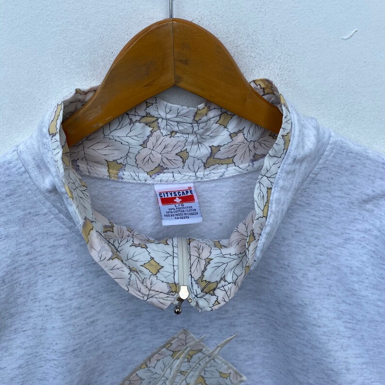 May include: A gray sweatshirt with a zipper and a floral print lining the collar. The label reads "CITYSCAPE" and includes the size "L/XL" and the fabric content "100% COTTON / COTON 100%".