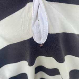 May include: Close-up of a black and white striped shirt with a white collar. The collar has a small hole in the center.