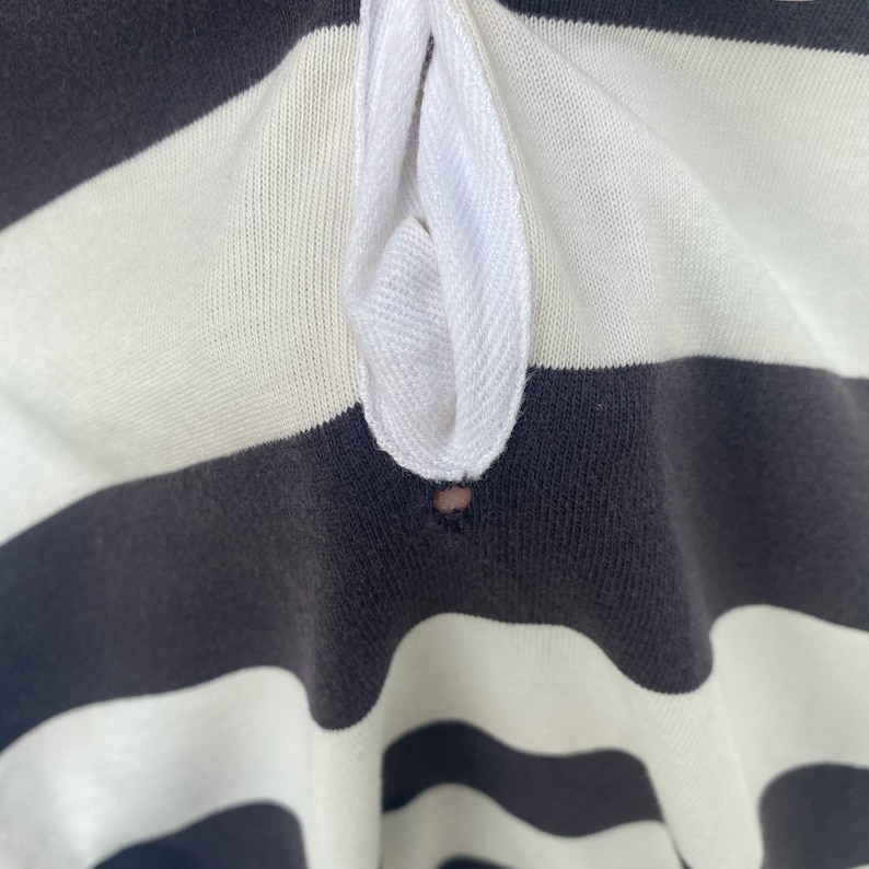 May include: Close-up of a black and white striped shirt with a white collar. The collar has a small hole in the center.