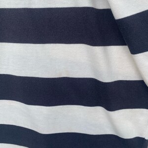 May include: Close-up of a white and navy blue striped fabric. The fabric is soft and has a subtle texture.