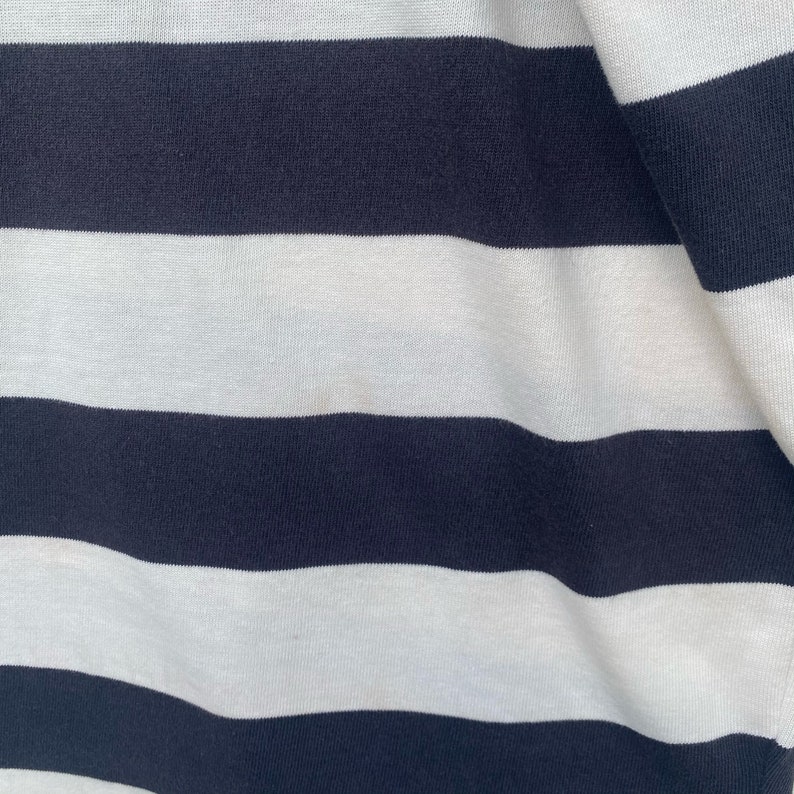 May include: Close-up of a white and navy blue striped fabric. The fabric is soft and has a subtle texture.