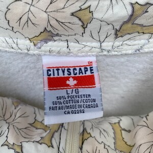 May include: White sweatshirt with a red and white label that says "CITYSCAPE" and "L/G 50% POLYESTER 50% COTTON/COTON FAIT AU/MADE IN CANADA CA 02282". The sweatshirt has a white and yellow floral pattern.