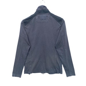 May include: A dark gray long-sleeved jacket with a zipper closure and a black patch on the back that says "HELLY HANSEN" and "HH" in a circle with "AVIREX 2016" underneath.