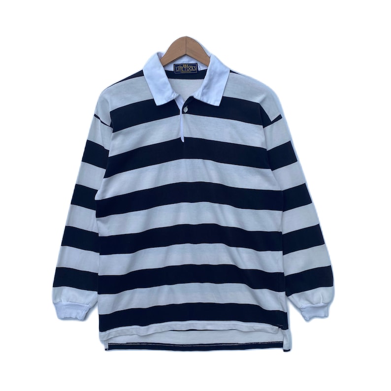 May include: A black and white striped long-sleeve rugby shirt with a white collar and a button closure. The shirt has the text "Life Tools" on the collar.