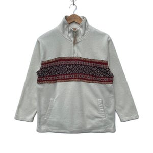 May include: A cream-colored fleece pullover with a high collar and a quarter-zip closure. The pullover features a horizontal band of patterned design in burgundy, red, and tan across the chest. It has two front pockets and long sleeves.