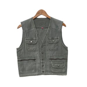 Peut inclure: Un gilet utilitaire en toile vert avec plusieurs poches et une fermeture boutonnée.