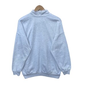 May include: A light gray sweatshirt with a mock neck and a zipper. The sweatshirt has a relaxed fit and long sleeves.