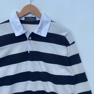 May include: A long-sleeved striped polo shirt with a white collar and a button closure. The shirt is black and white with horizontal stripes. The shirt has a label that reads "Life Tools" on the front.