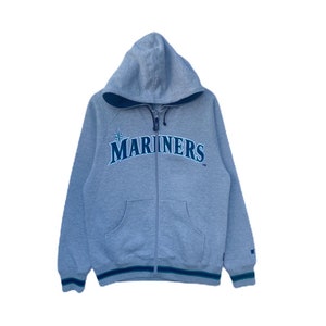May include: A gray hooded sweatshirt with a navy blue and green Mariners logo on the front. The sweatshirt has a zipper closure and a pocket on the front.