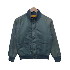 May include: A dark green bomber jacket with a snap closure and multiple pockets. The jacket has a ribbed collar and cuffs.