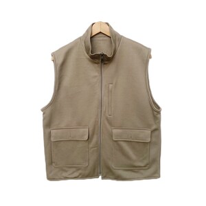 May include: A tan sleeveless zip-up vest with two large pockets on the front. The vest has a stand-up collar and a zipper closure.