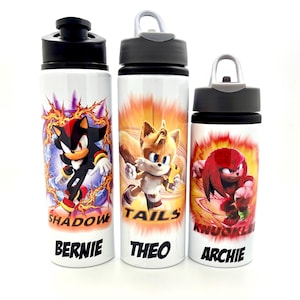 May include: Three white water bottles with black lids and carrying handles. Each bottle features a different Sonic the Hedgehog character: Shadow, Tails, and Knuckles. The bottles are personalised with the names Bernie, Theo, and Archie.