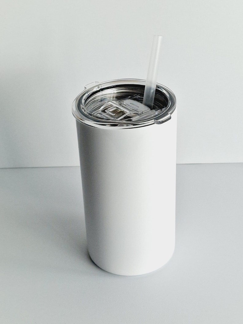 Pode incluir: Um copo de a&ccedil;o inoxid&aacute;vel branco com uma tampa transparente e um canudo de pl&aacute;stico transparente. O copo est&aacute; vazio.