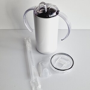 Pode incluir: Um copo de a&ccedil;o inoxid&aacute;vel branco com duas al&ccedil;as, uma tampa transparente com um furo para canudo e um canudo transparente. O copo est&aacute; sobre uma superf&iacute;cie branca.