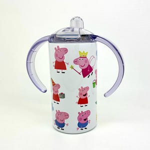 Pode incluir: Um copo de a&ccedil;o inoxid&aacute;vel branco com tampa e al&ccedil;as roxas. O copo apresenta um padr&atilde;o repetido de personagens do Peppa Pig em v&aacute;rias poses.