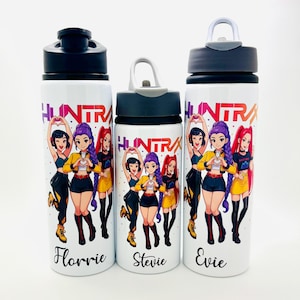 May include: Three white water bottles with black lids and the word "HUNTRA" in a rainbow gradient. Each bottle features a cartoon illustration of four girls. The names "Florrie", "Stevie", and "Evie" are printed on the bottles.
