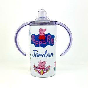 Pode incluir: Copo de a&ccedil;o inoxid&aacute;vel branco com al&ccedil;as roxas e tampa transparente. O copo apresenta um design de Peppa Pig com o nome "Jordan" impresso no lado.