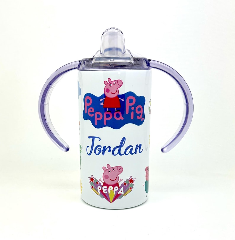 Pode incluir: Copo de a&ccedil;o inoxid&aacute;vel branco com al&ccedil;as roxas e tampa transparente. O copo apresenta um design de Peppa Pig com o nome "Jordan" impresso no lado.