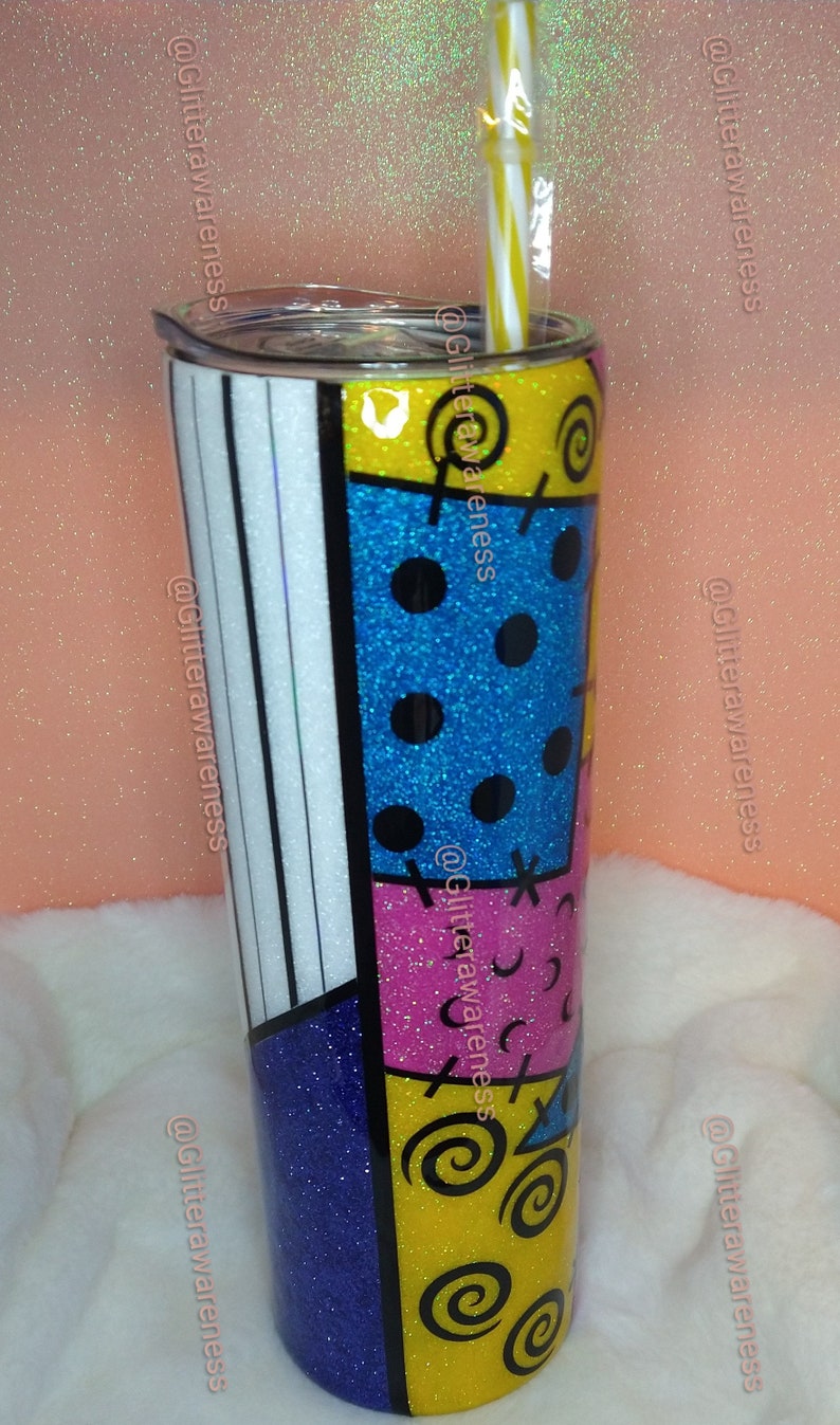 May include: A glitter-covered tumbler with a colorful patchwork design. The tumbler features sections of blue, yellow, pink, and white, with black accents and a striped straw. The design is reminiscent of a character's outfit.