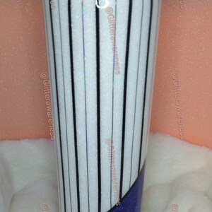 May include: A tall, insulated tumbler with a white background and vertical black stripes. The bottom third of the tumbler is a deep blue glitter. A yellow and white striped straw is visible.