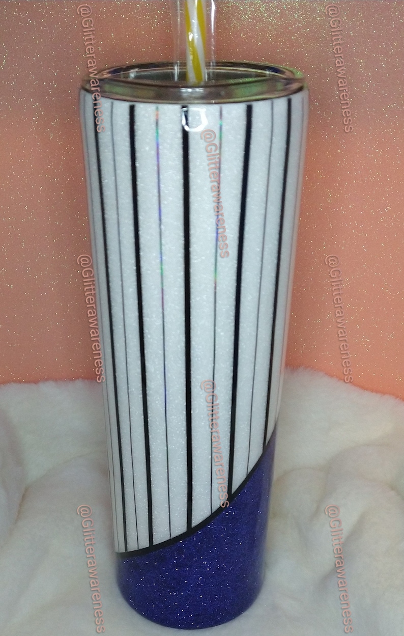 May include: A tall, insulated tumbler with a white background and vertical black stripes. The bottom third of the tumbler is a deep blue glitter. A yellow and white striped straw is visible.