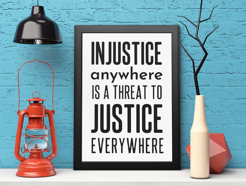 Puede incluir: Impresi&oacute;n enmarcada en negro con el texto "INJUSTICE anywhere IS A THREAT TO JUSTICE EVERYWHERE" sobre fondo blanco. La impresi&oacute;n est&aacute; en un estante blanco con una linterna roja y un jarr&oacute;n blanco con una rama.