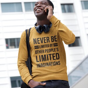 Puede incluir: Una sudadera de color amarillo mostaza con el texto "NEVER BE LIMITED BY OTHER PEOPLE'S LIMITED IMAGINATIONS" impreso en negro.