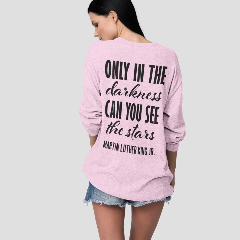 Puede incluir: Sudadera rosa de manga larga con la cita "ONLY IN THE darkness CAN YOU SEE the stars" de Martin Luther King Jr. impresa en la espalda.
