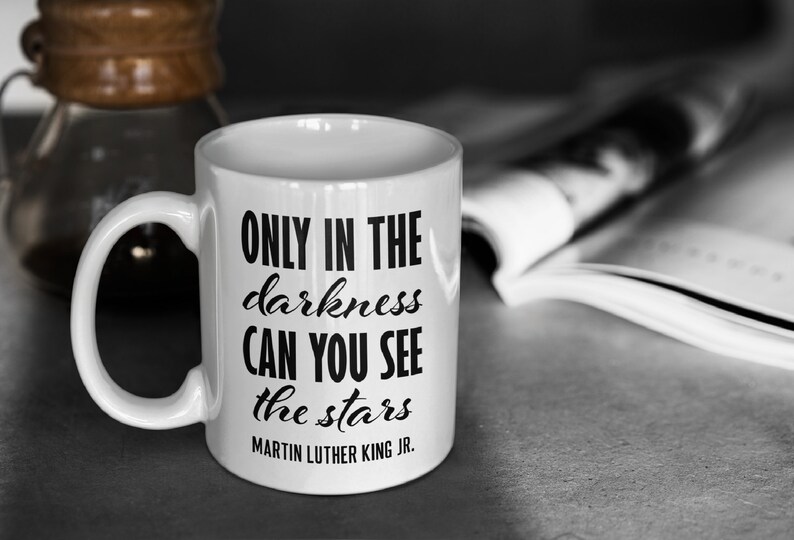 Puede incluir: Taza de caf&eacute; de cer&aacute;mica blanca con una cita en negro que dice "Only in the darkness can you see the stars - Martin Luther King Jr."