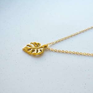 Peut inclure: Un collier en or avec une cha&icirc;ne d&eacute;licate et un pendentif en forme de feuille. Le pendentif est une d&eacute;coupe d&eacute;taill&eacute;e d'une feuille de monstera.