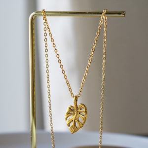 Peut inclure: Un collier en or avec une cha&icirc;ne d&eacute;licate et un pendentif en forme de feuille de monstera.