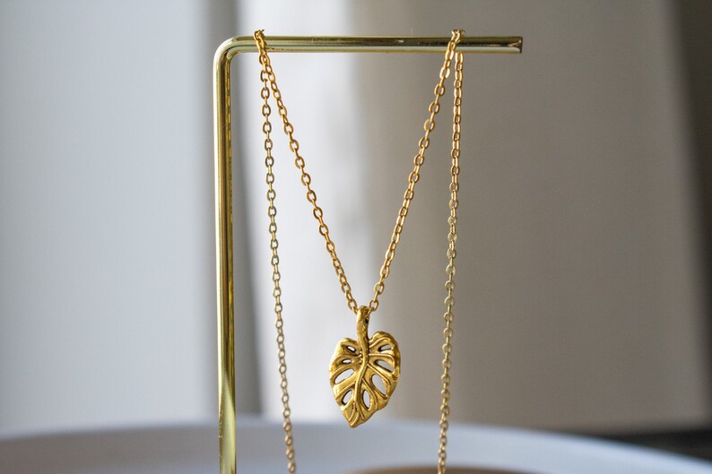 Peut inclure: Un collier en or avec une cha&icirc;ne d&eacute;licate et un pendentif en forme de feuille de monstera.